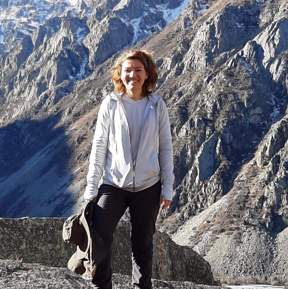 A full body image of Nasima, a woman with dark blonde hair. Standing in a mountain range