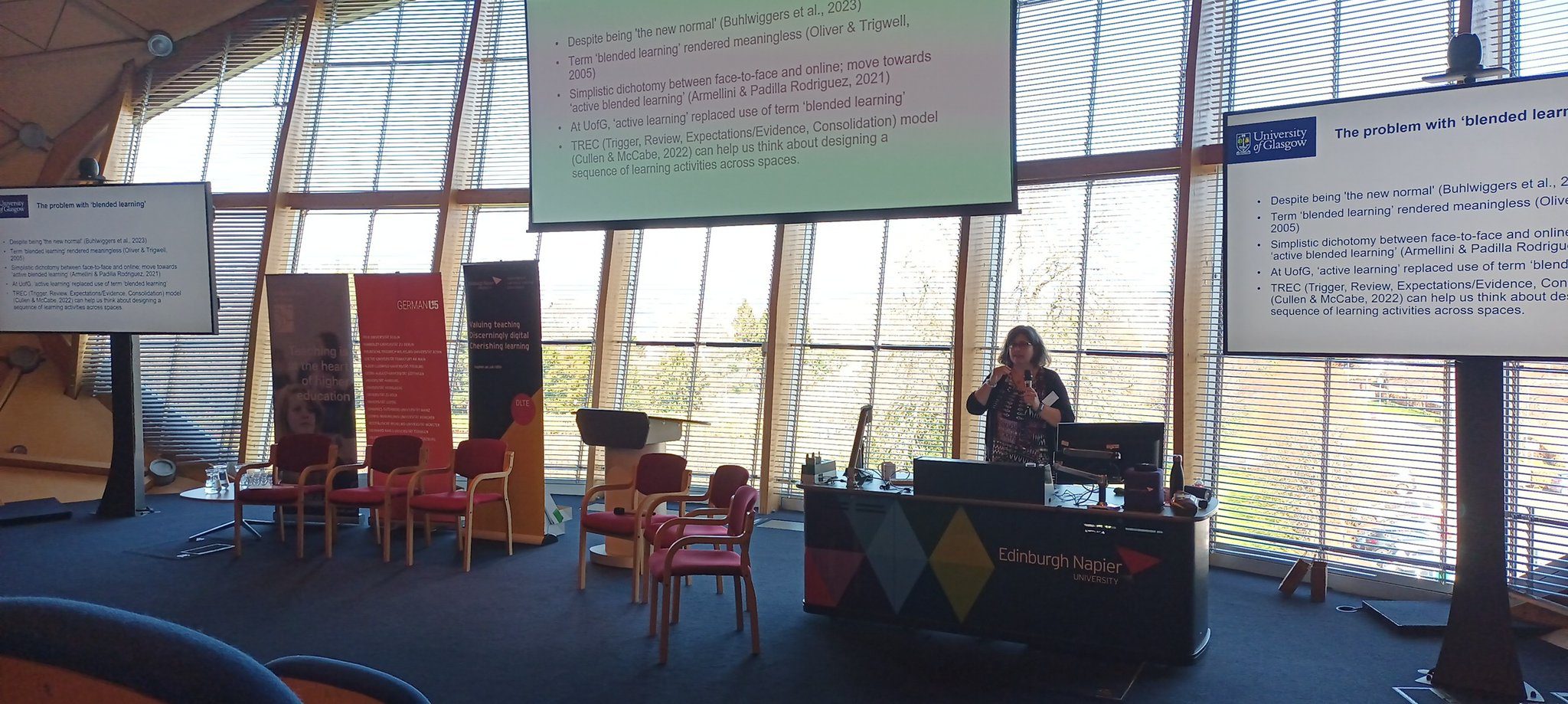 Dr Vicki Dale talking about "The Problem with 'Blended Learning'". The slide onscreen has 5 bullet points. 1: Despite being 'the new normal' (Buhlwiggers et al., 2023) 2: the term 'blended learning' is rendered meaningless (Oliver & Trigwell, 2005). 3: It is a simplistic dichotomy between face to face and online; move towards 'active blended learning' (Armellini & Padilla Rodriguez, 2021). 4: At University of Glasgow, 'active learning' replaced use of the term 'blended learning'. 5: TREC (Trigger, Review, Expecations/Evidence, Consolidation) model (Cullen & McCabe, 2022) can help us think about designing a sequence of learning activities across spaces.