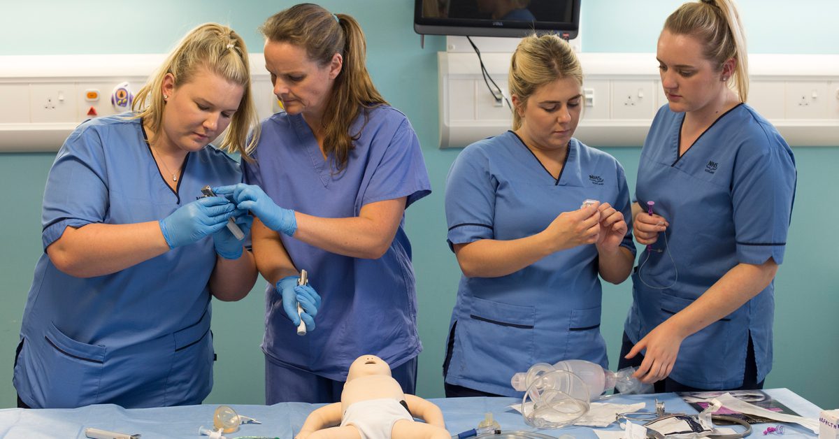Midwifery students working together in the clinical skills centre, wearing their scrub uniforms.