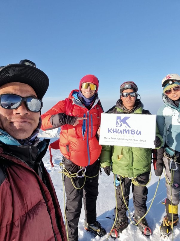 The group is seen during their ascent with snow on the ground. They are wearing jackets and climbing gear, and one member is holding a sign.  