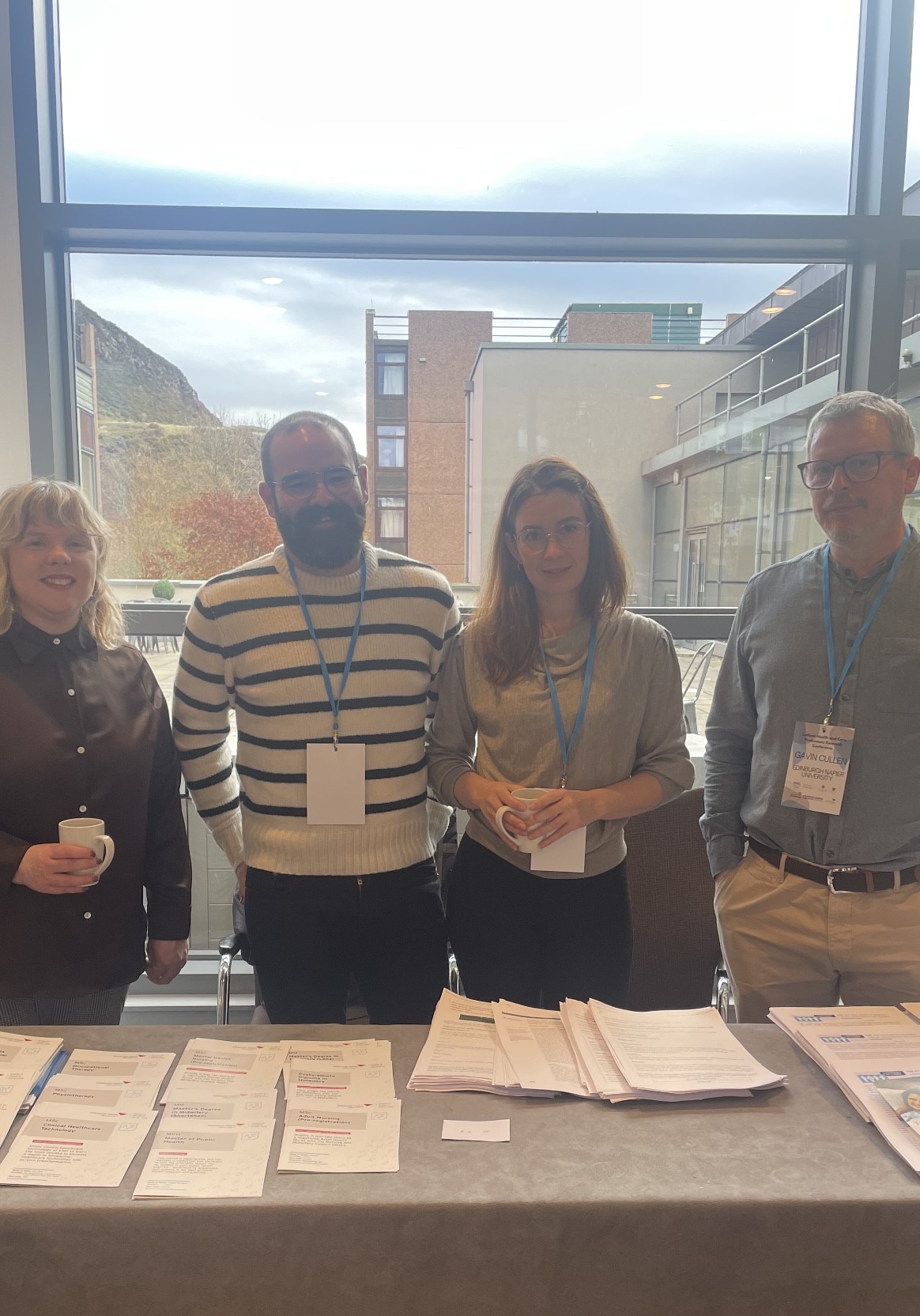 Group image of Edinburgh Napier School of Health and Social Care academics at a desk in front of a window attending a conference.