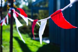 Red and white bunting is fluttering in the breeze. There is green brass and the outline of a building in the background.