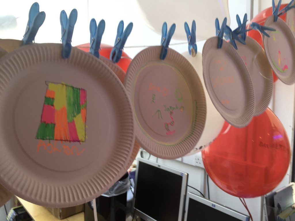 Paper plates, with pictures drawn on by children, and hanging on a washing line attached by pegs.