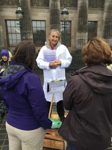 A woman wearing a lab coat stands on a soapbox with a crowd in front of her