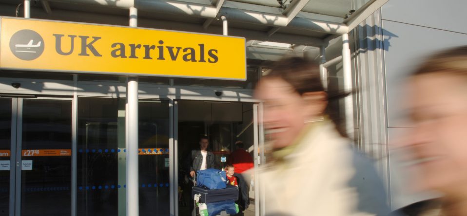 Passengers walking by the UK arrivals door at an airport.