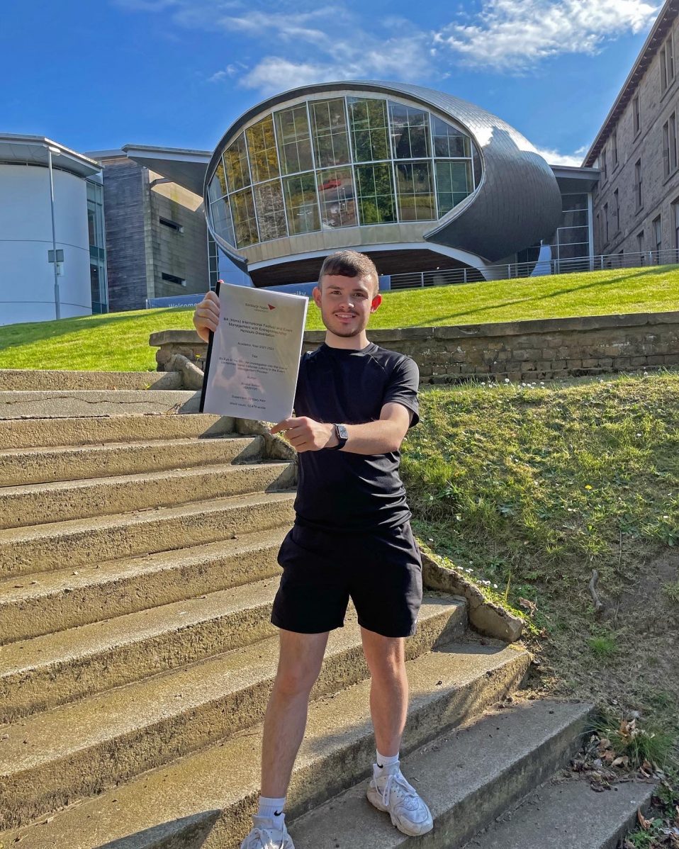Brodie Sutton standing outside the Craiglockhart campus, holding up his dissertation