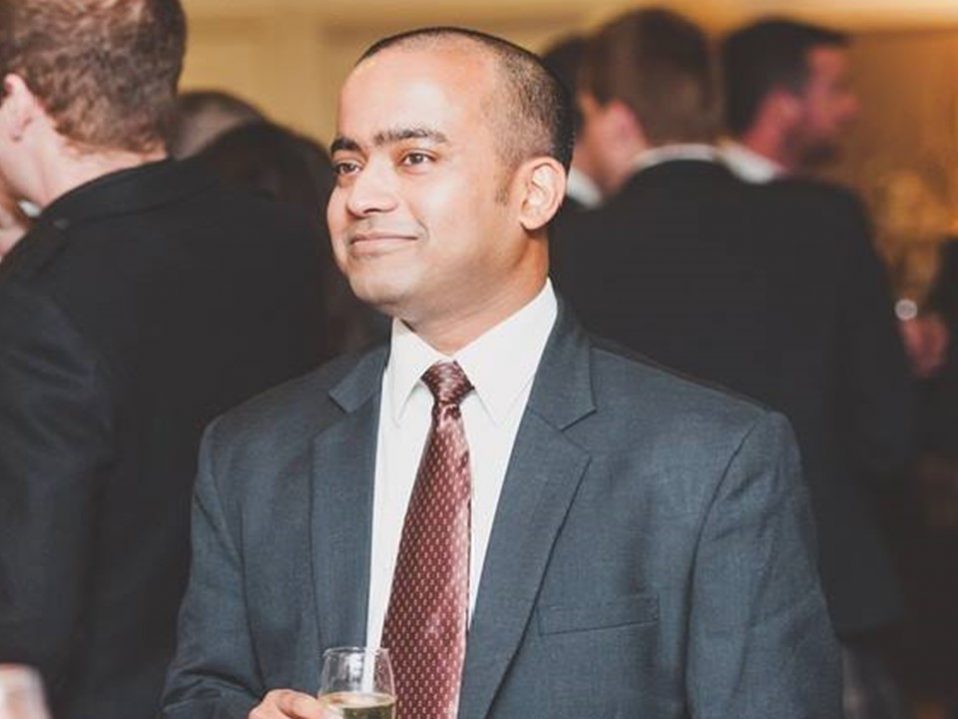 Sam Matthew at an event, wearing a suit, holding a class of champagne.