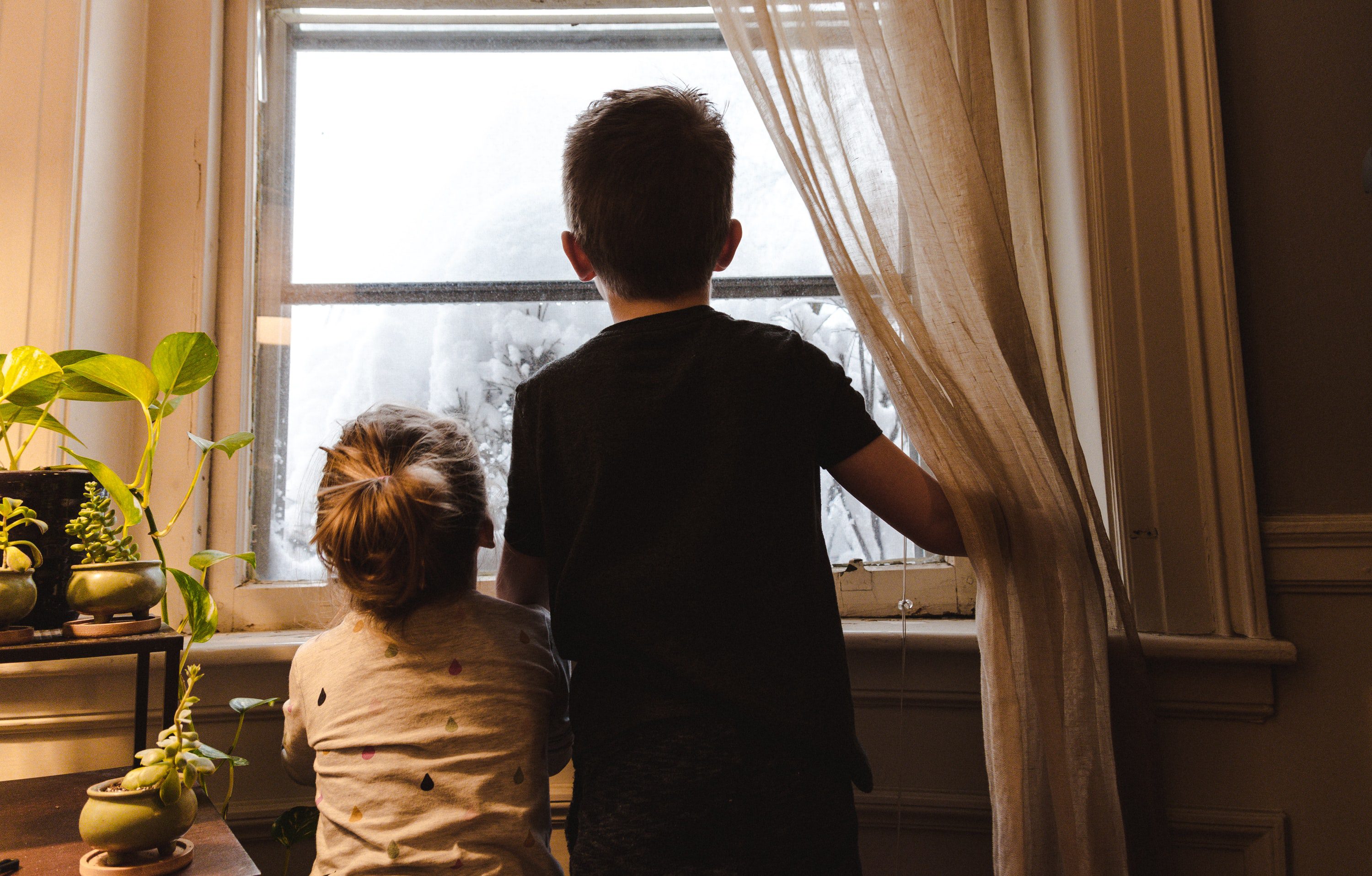 Two children photographed from behind, looking out the window