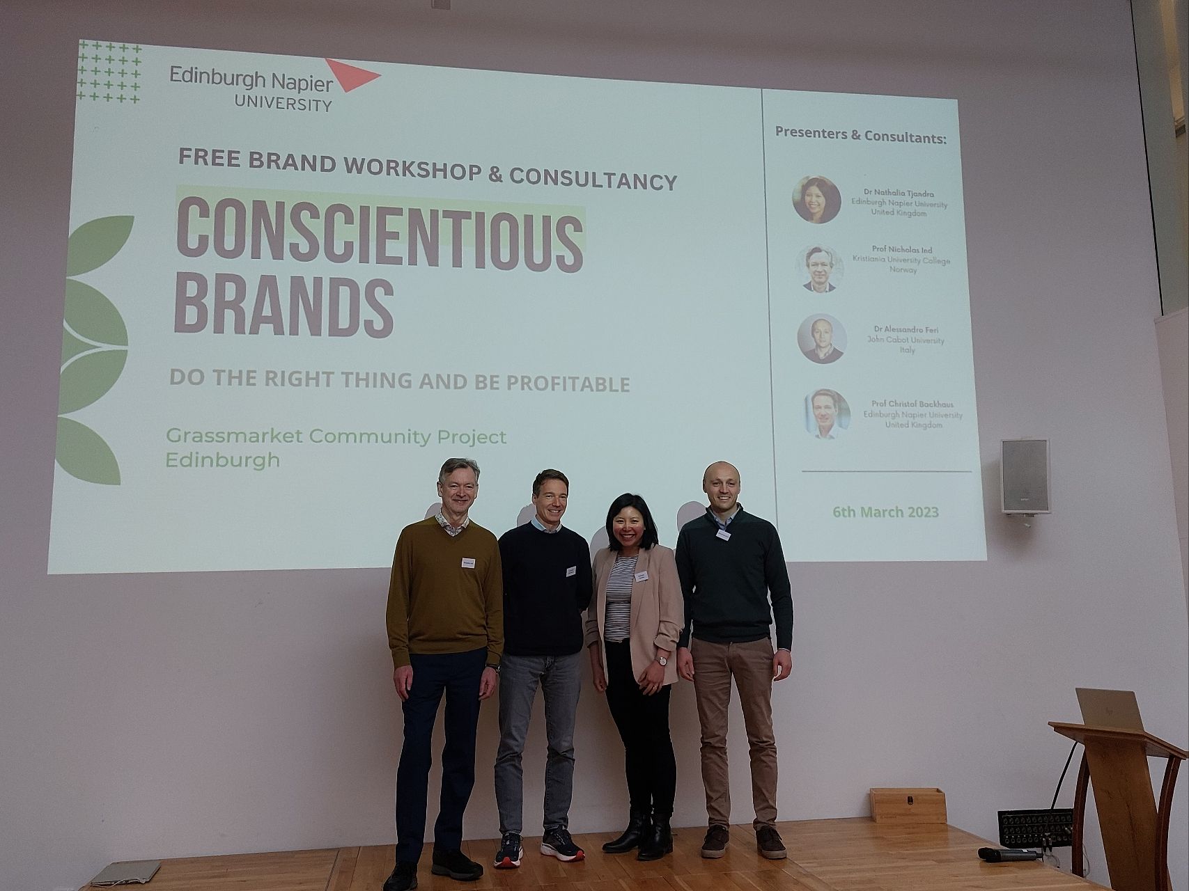 The academic team with Nicholas, Christof, Nathalia and Alessandro standing on a stage in front of their presentation