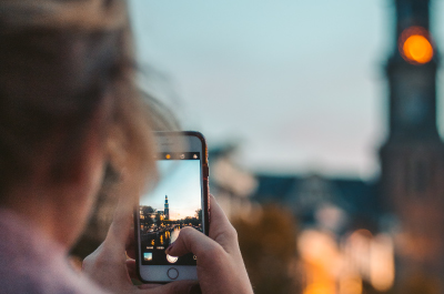 Person taking a picture on their mobile phone of the city as the sun sets.